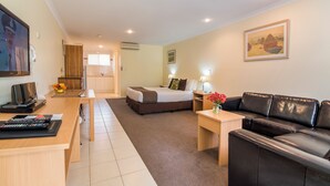 A hotel room with a bed, a desk with a computer, a black leather sofa, and a small table with flowers. - Emu Point Motel & Apartments (Emu Point)