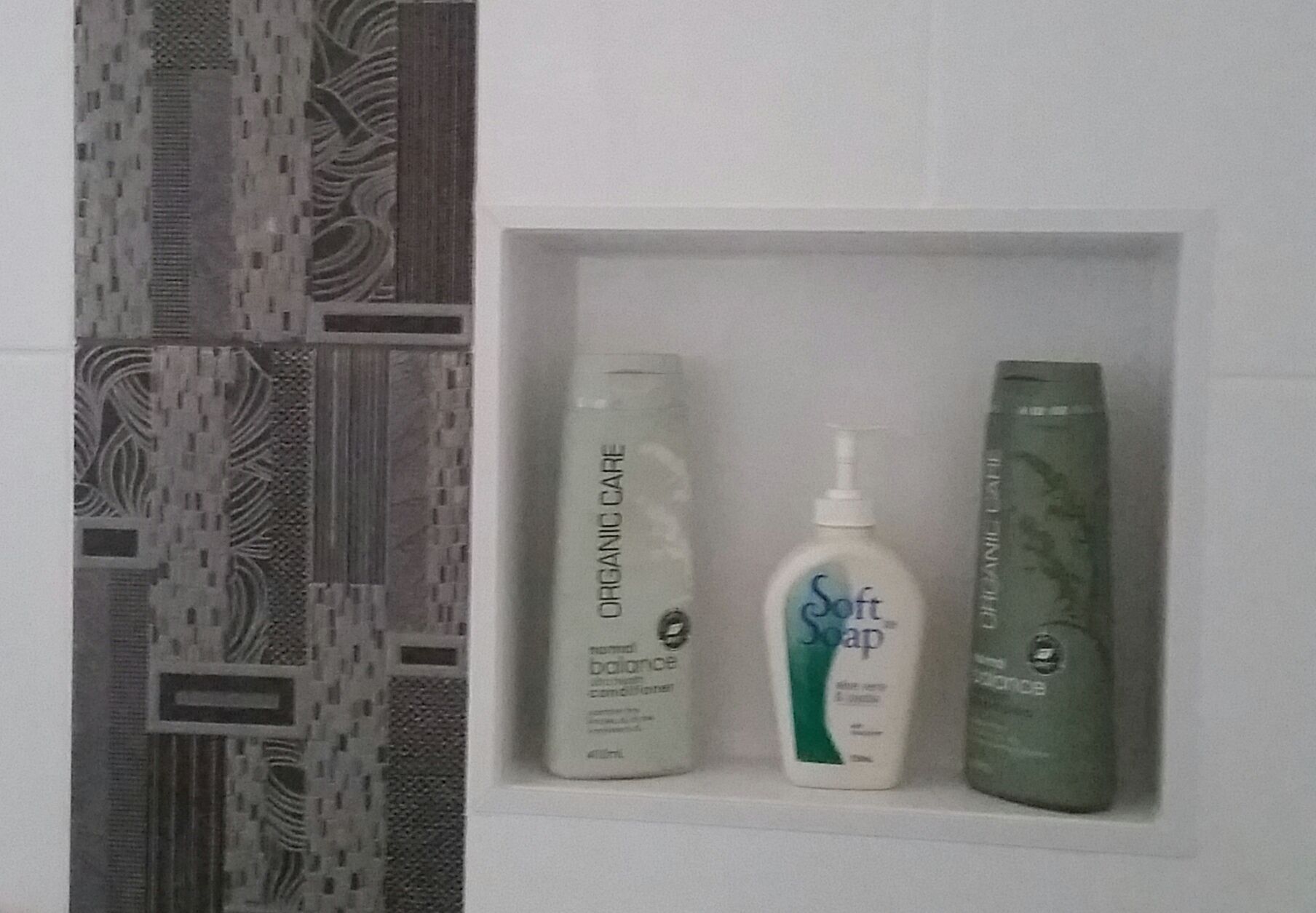 A bathroom shelf with three toiletry bottles: a white bottle labeled "Organic Care," a white bottle labeled "Soft Soap," and a green bottle labeled "Balance."