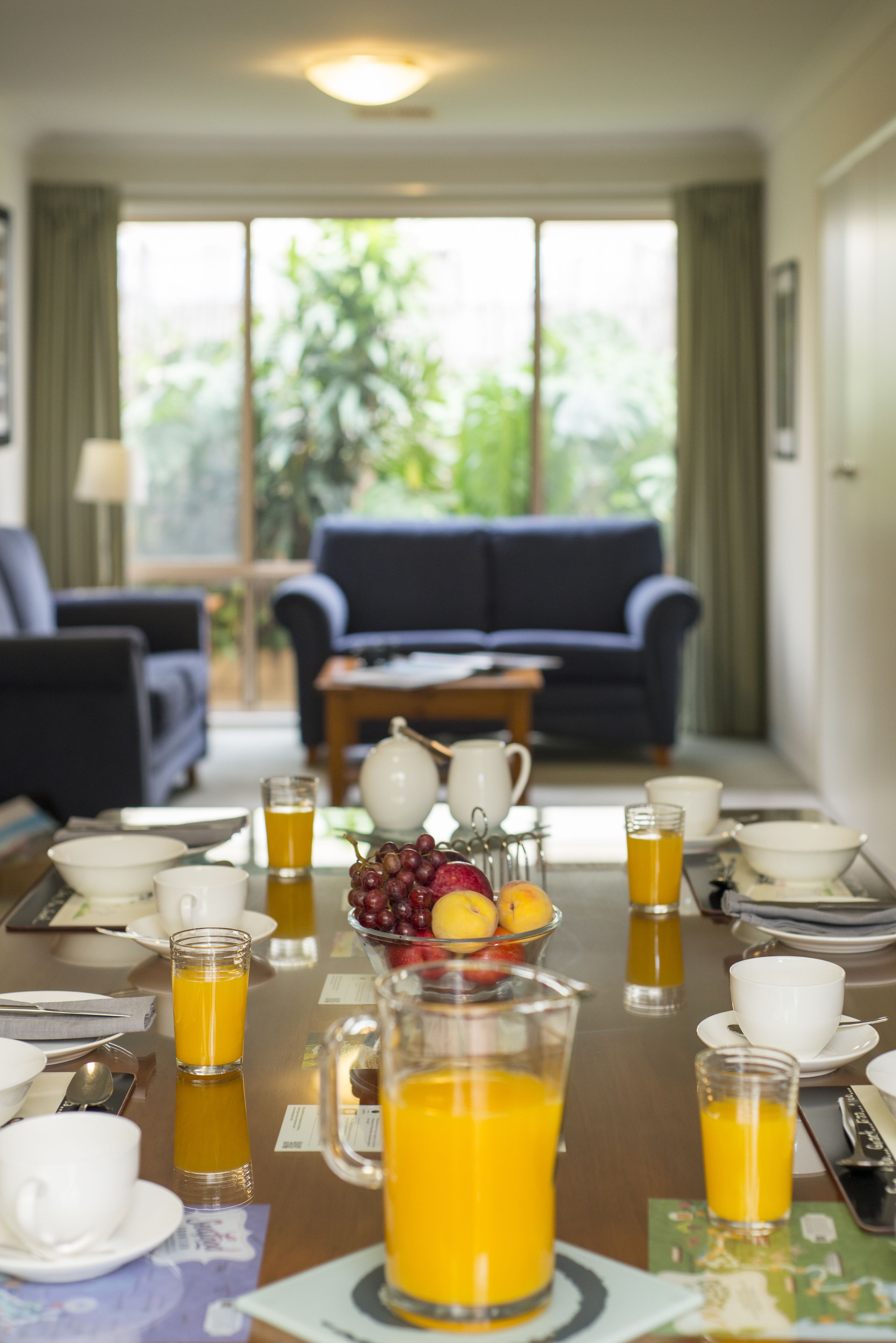 A breakfast setting with a table set for two, including plates, cups, and a pitcher of orange juice.