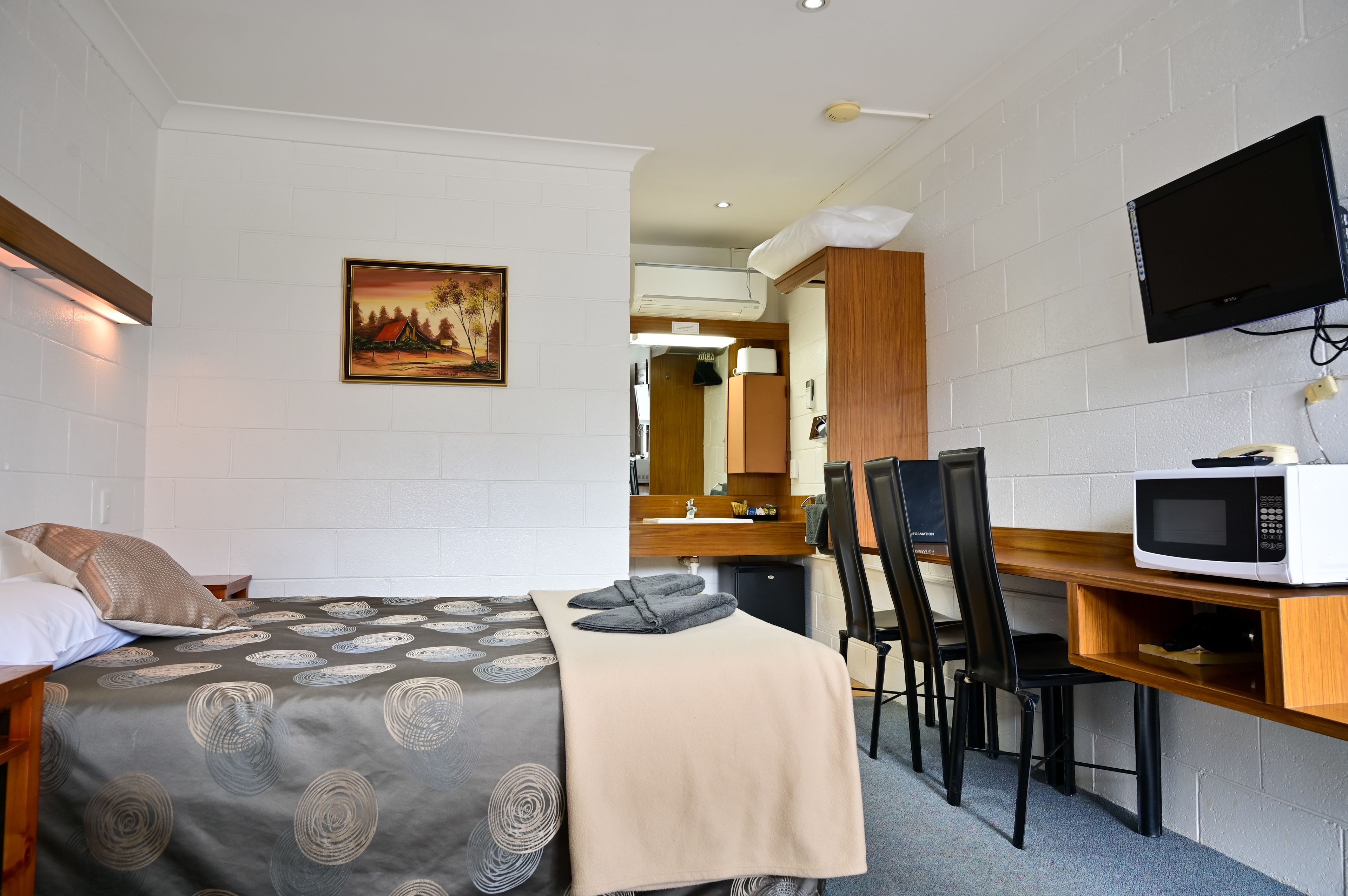 Une chambre d’hôtel avec un lit, un bureau doté d’un micro-ondes, une télévision et un tableau accroché au mur.