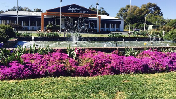A building with a 'buyer motor inn' sign, surrounded by a fountain and vibrant purple flowers. - Byer Fountain Motor Inn, Holbrook (Holbrook)