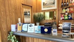 A hotel reception desk with various awards and certificates displayed, a potted plant, and a selection of snacks and beverages. - Byer Fountain Motor Inn, Holbrook (Holbrook)