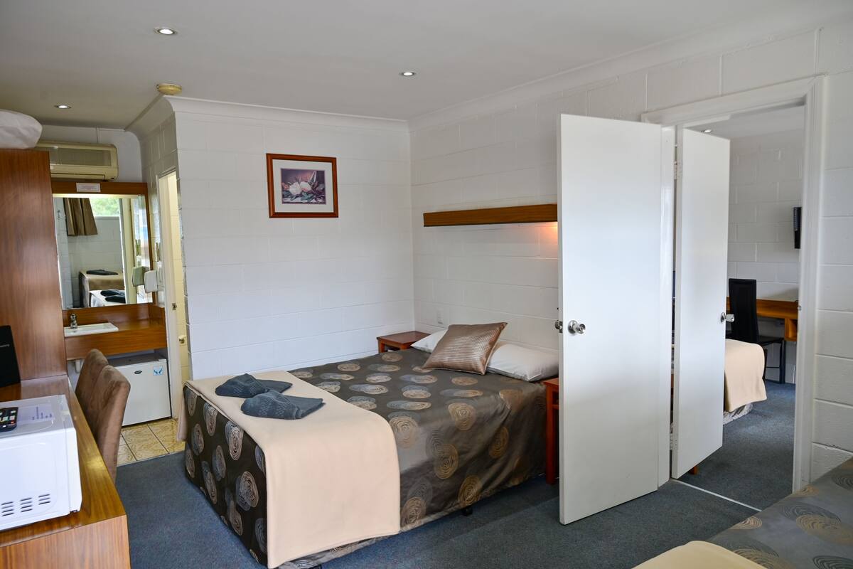 A compact bedroom with a bed, bedside table, and a desk with a computer.