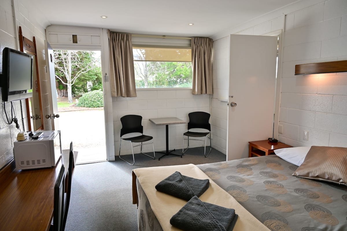 A hotel room with a bed, a desk with a microwave, two chairs, a small table, and a TV mounted on the wall.