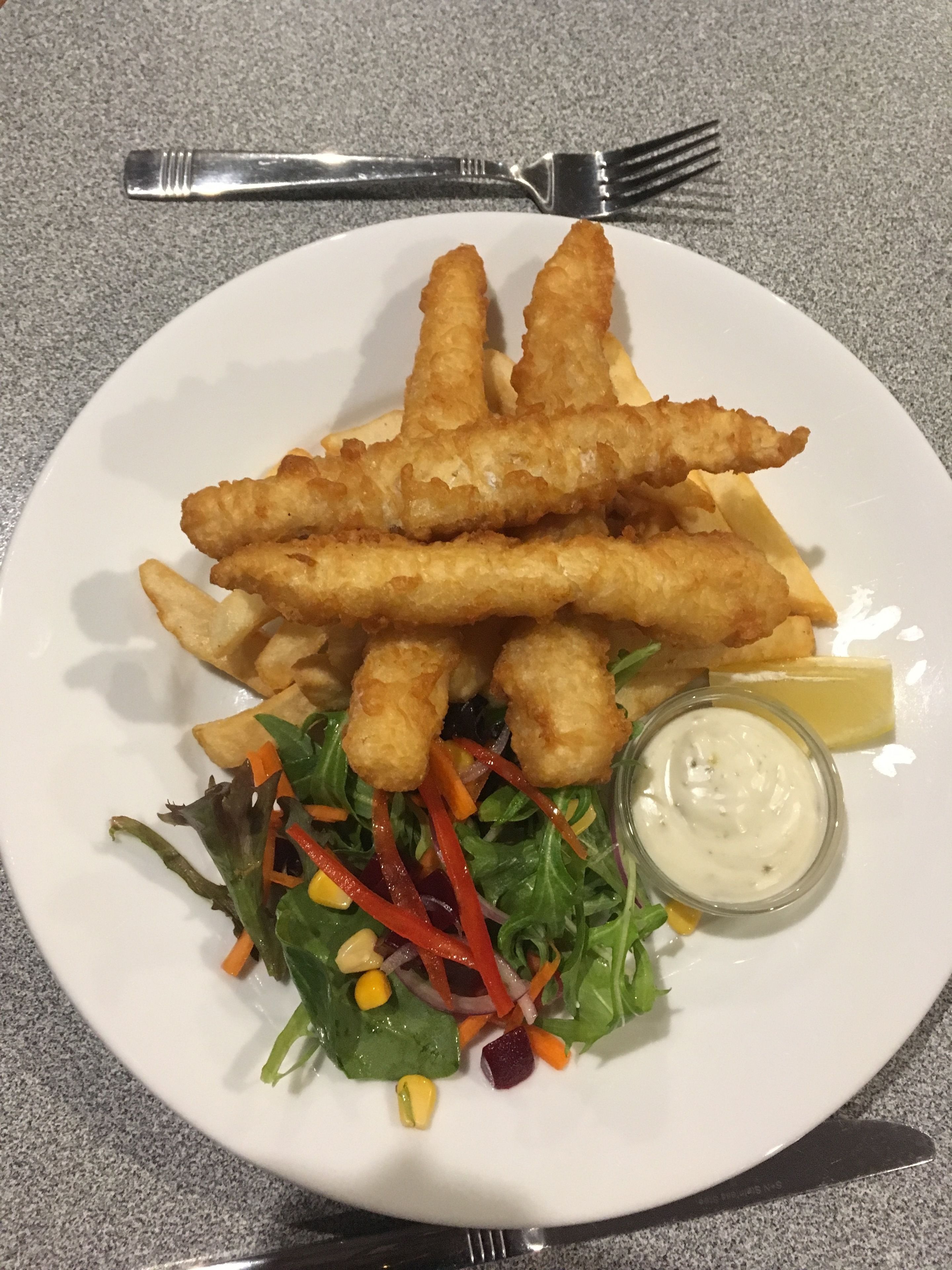 A plate with fish and chips, a salad, and a small bowl of sauce.