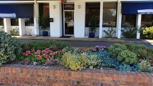 A building with a brick planter with various plants and flowers. - Byer Fountain Motor Inn, Holbrook (Holbrook)