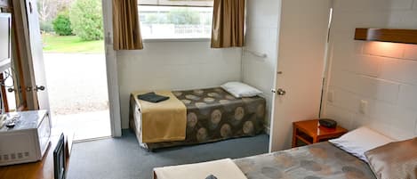 A single room with a bed, a desk, a chair, a window with curtains, and a door.