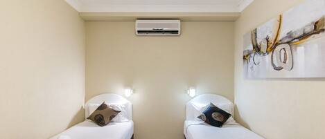 A hotel room with two beds, each with patterned bedding and towels, a ceiling air conditioner, and a wall-mounted artwork.