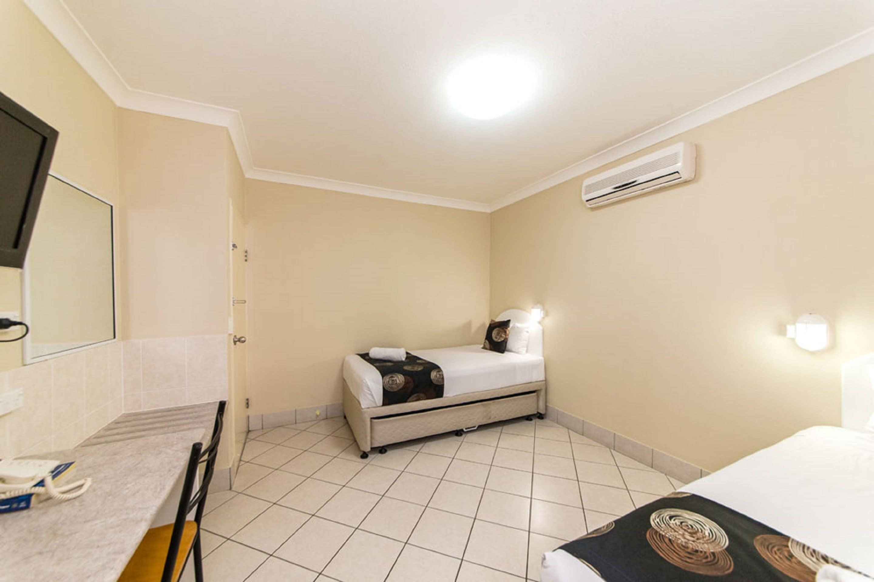 A hotel room with a bed, a desk with a telephone, and a wall-mounted air conditioner.