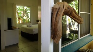 A room with a bed, a small table, and a window with a view of greenery. - Villa Marine Holiday Apartments (Yorkeys Knob)