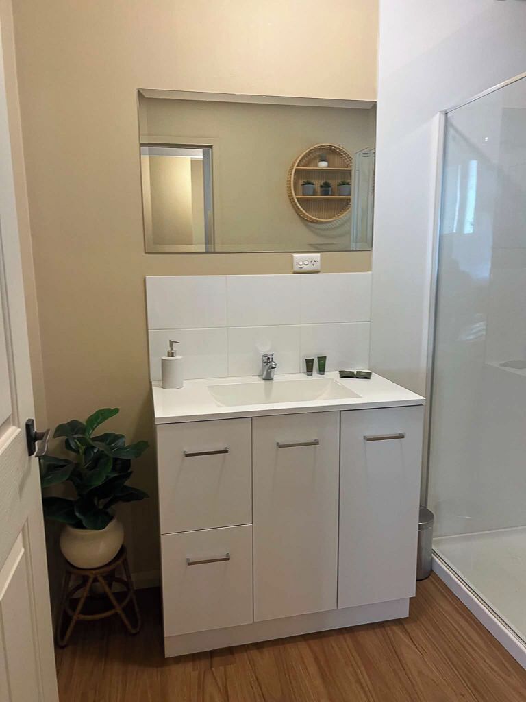 A bathroom with a white sink, mirror, and cabinets.