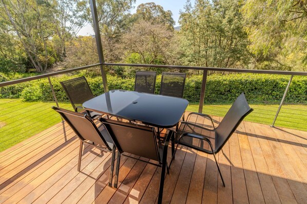 A deck with a table and chairs, surrounded by a metal railing, overlooking a well-maintained garden.