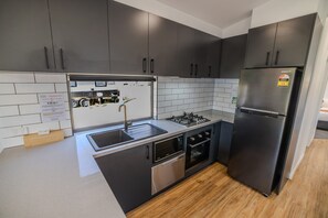 A modern kitchen with dark cabinets, a stainless steel refrigerator, a built-in oven, and a sink. - Porepunkah Pines Holiday Park (Porepunkah)