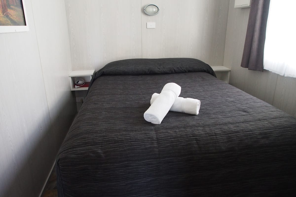 A neatly made bed with a dark gray bedspread and two rolled white towels on it.