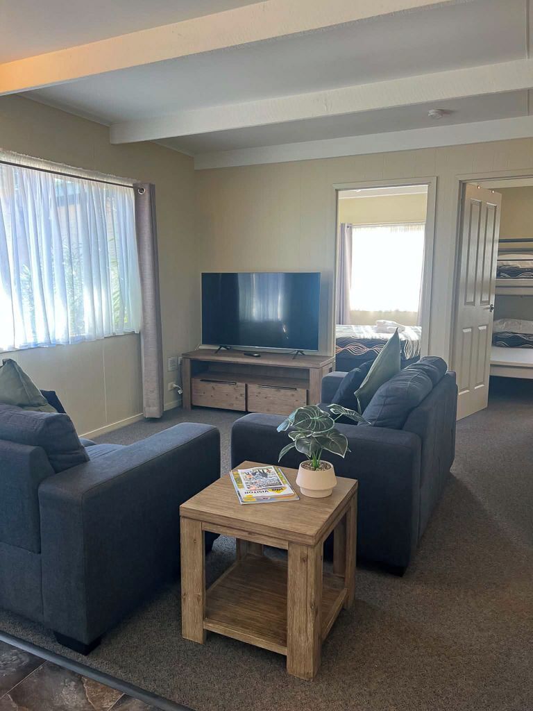 A living room with a sofa set, a television, a small wooden table with a plant, and a door leading to another room.