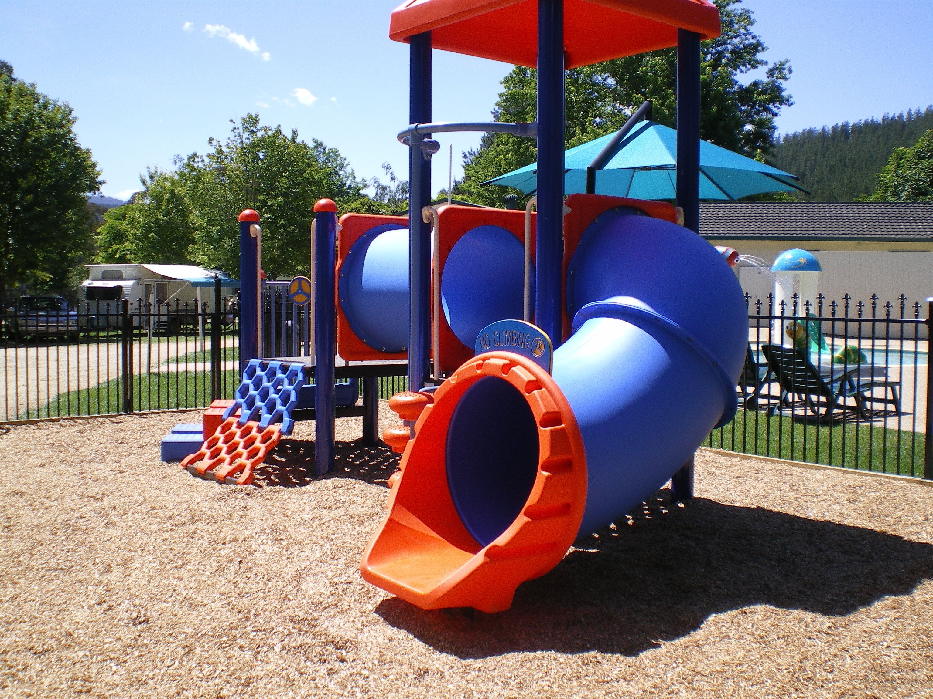 Un parque infantil con tobogán, zona de escalada y área de juegos cercada.