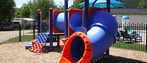 Un parque infantil con tobogán, zona de escalada y área de juegos cercada.