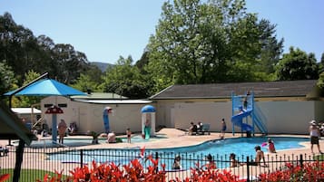 Guests can enjoy a refreshing swim in the pool surrounded by lush trees and a building with a tiled roof.