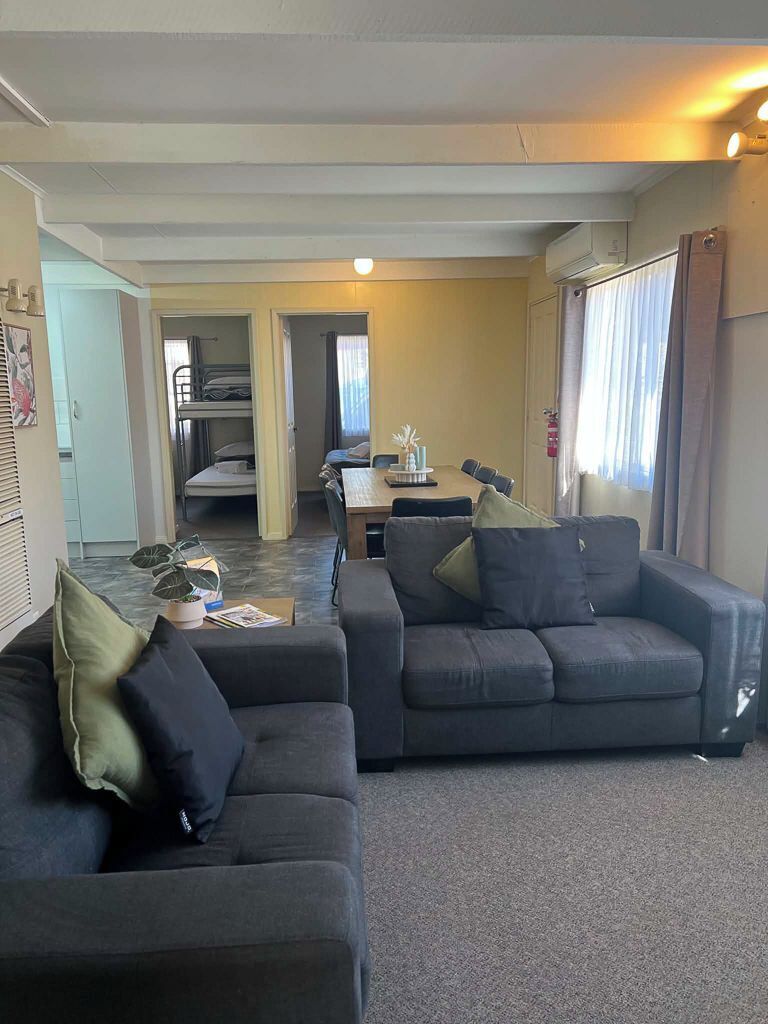 A living room with a sofa, a dining table, and a kitchen area in the background.