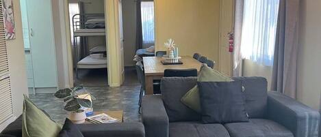 A living room with a sofa, a dining table, and a kitchen area in the background.