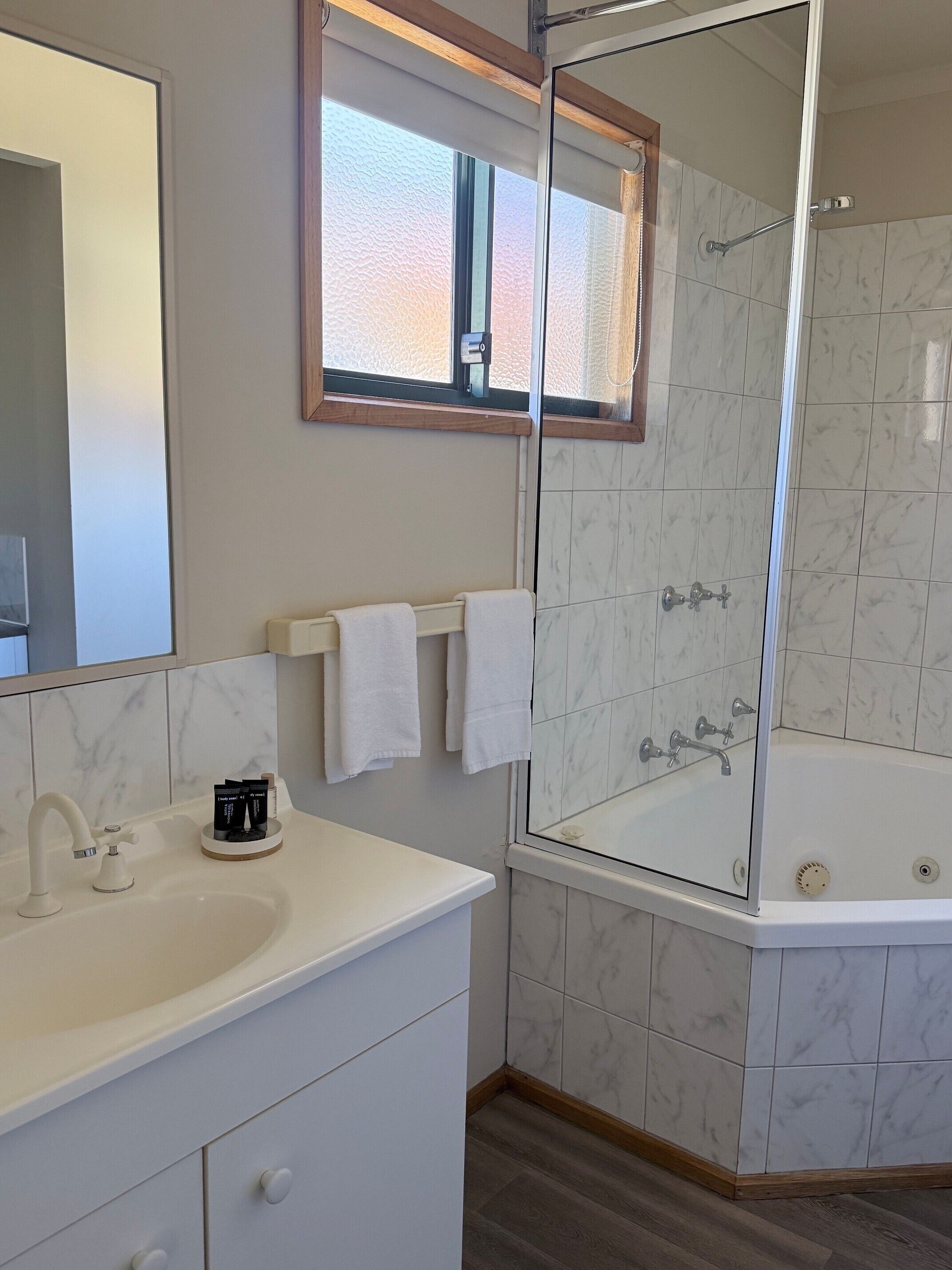 A modern bathroom with a white sink, a glass-enclosed shower, and a marble-tiled wall.