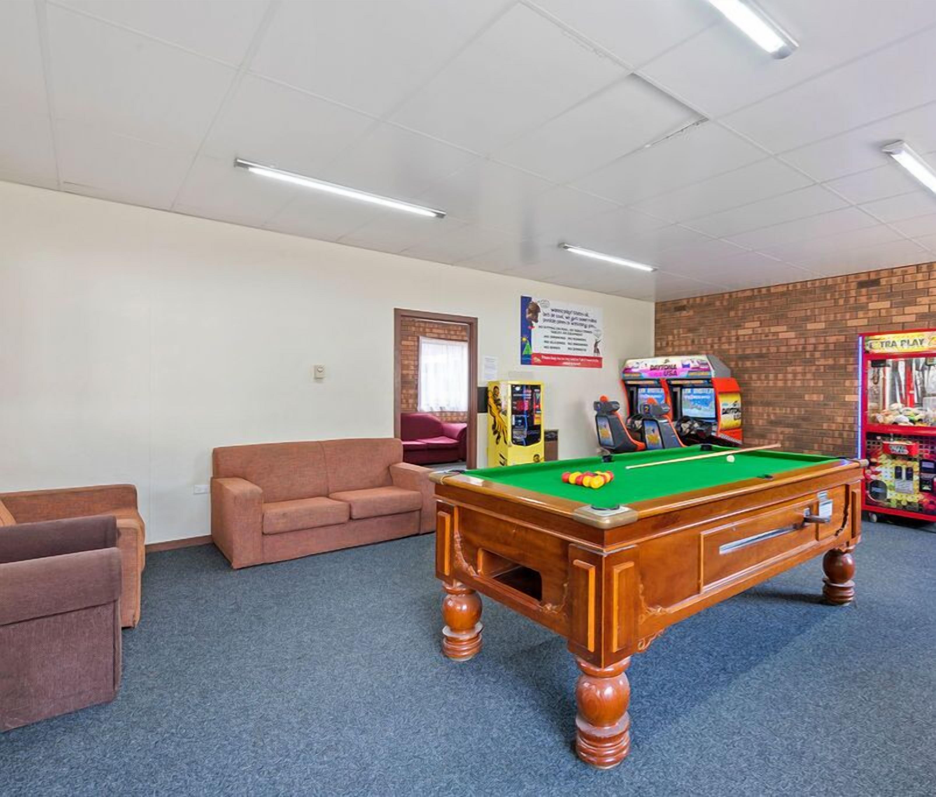 A pool table in a room with a brick wall, a red couch, and arcade games.