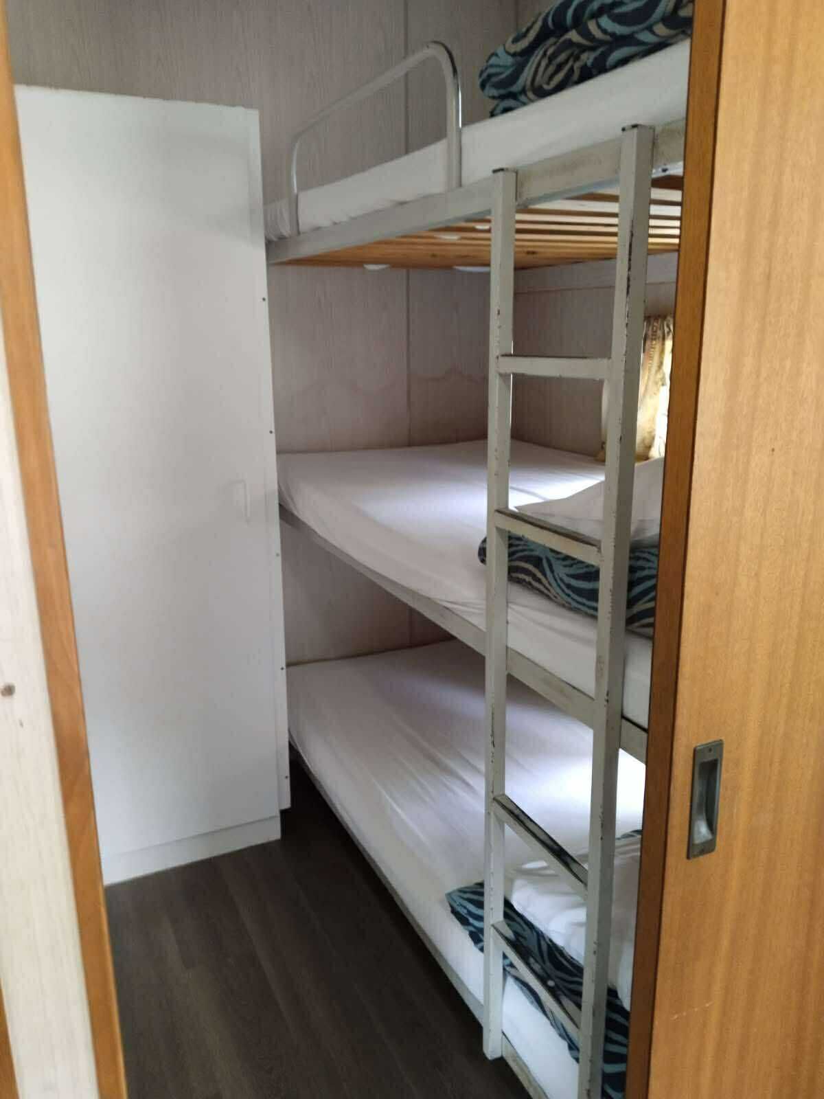 Un lit superposé à trois niveaux, une porte en bois et un plancher foncé.