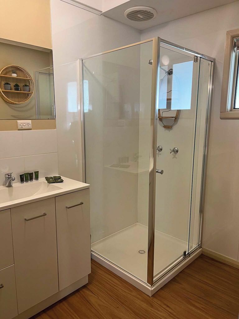 Une salle de bain moderne avec une douche à parois de verre, un meuble-lavabo blanc avec un miroir et un plancher en bois.