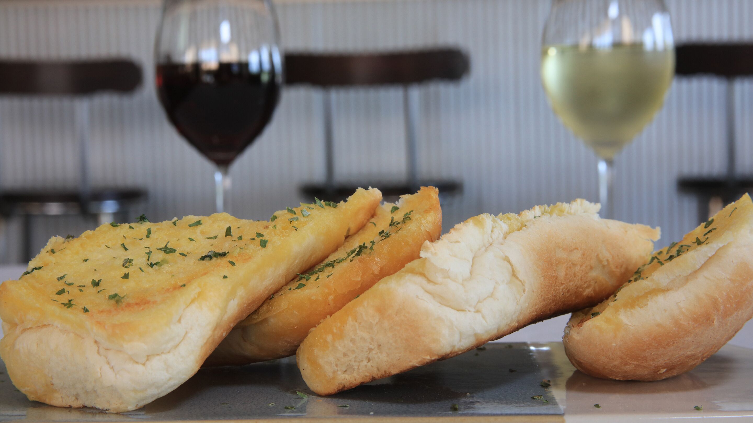 Tres rebanadas de pan con ajo, decoradas con hierbas, con dos copas de vino al fondo.