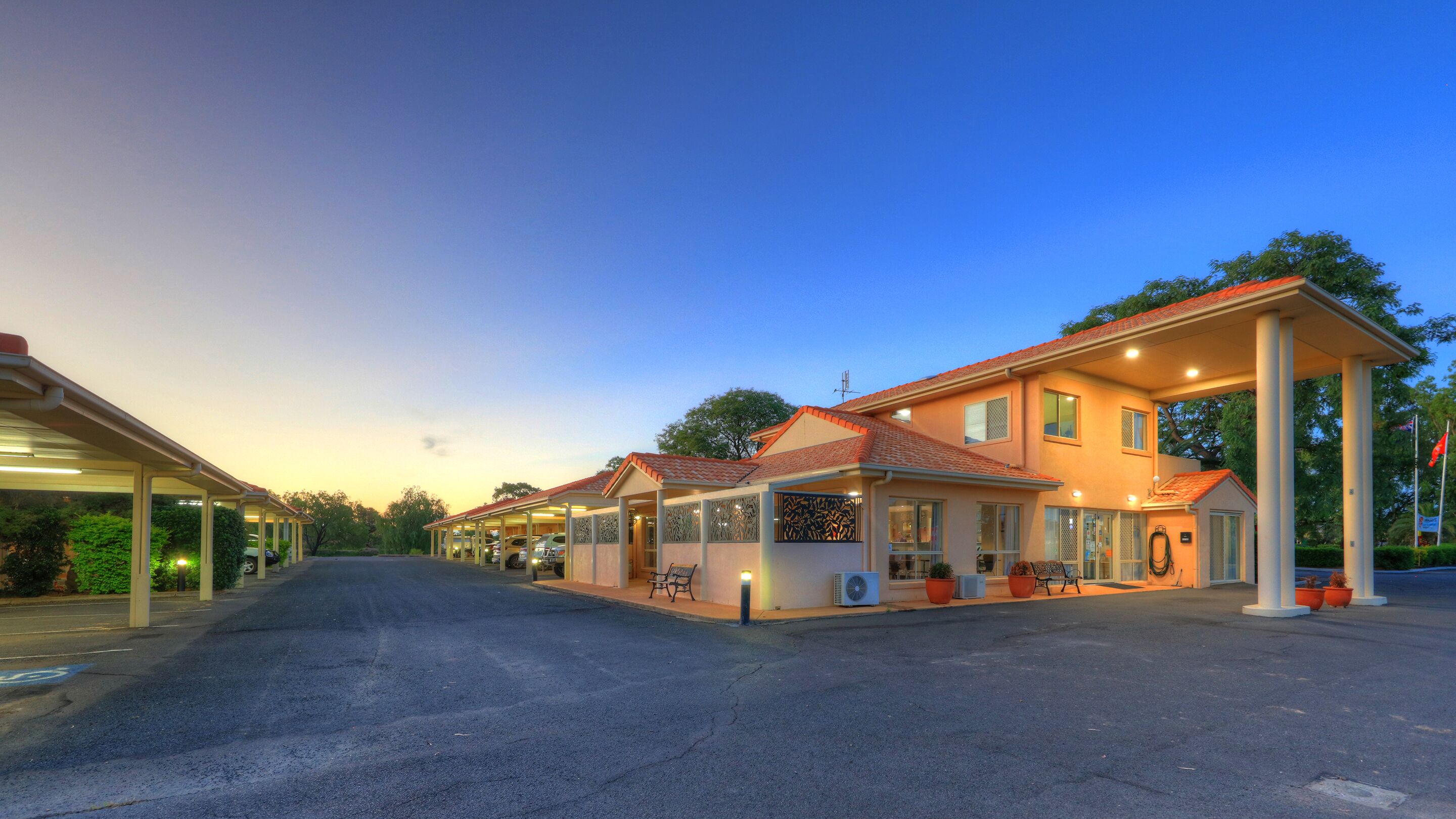 A well-lit, multi-story hotel with a covered parking area and outdoor seating.
