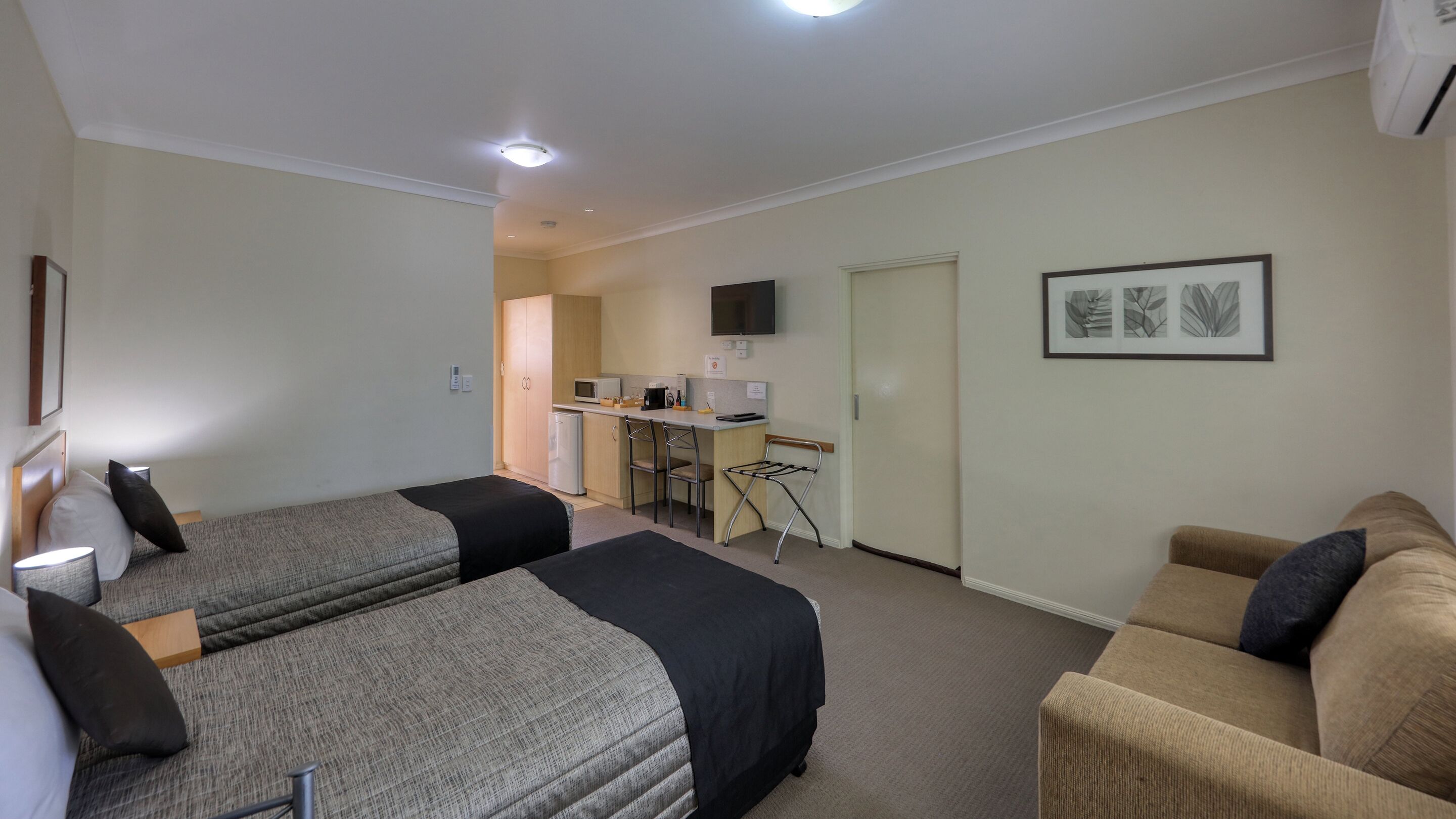 Una habitación de hotel con dos camas, una kitchenette, un televisor y una planta enmarcada en la pared.