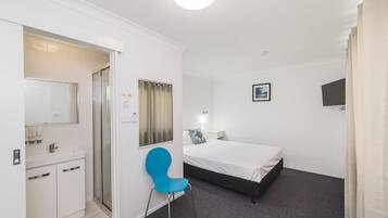 A bedroom with a bed, a chair, a bedside table, a TV, and a bathroom with a sink and mirror.