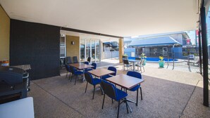 An outdoor patio area with tables and chairs, a covered seating area, and a view of a building with a blue roof. - Metro Motel Rockhampton (Rockhampton)