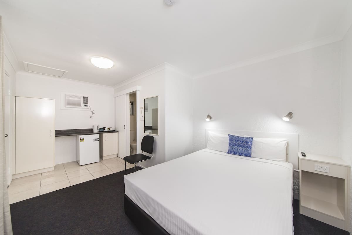 A hotel room with a bed, a desk, a chair, a wardrobe, and a nightstand.