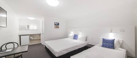 A hotel room with two beds, a desk, a chair, and a small kitchenette.