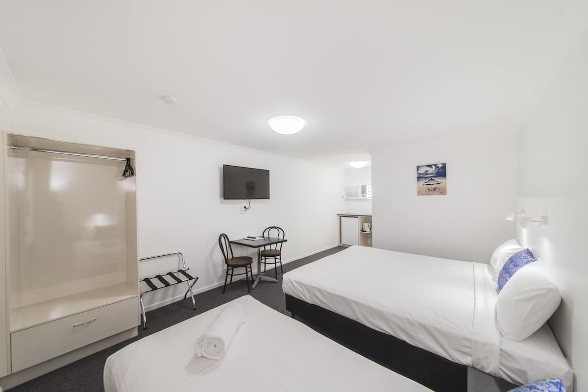 A hotel room with two single beds, a desk with a chair, a TV mounted on the wall, and a wardrobe.