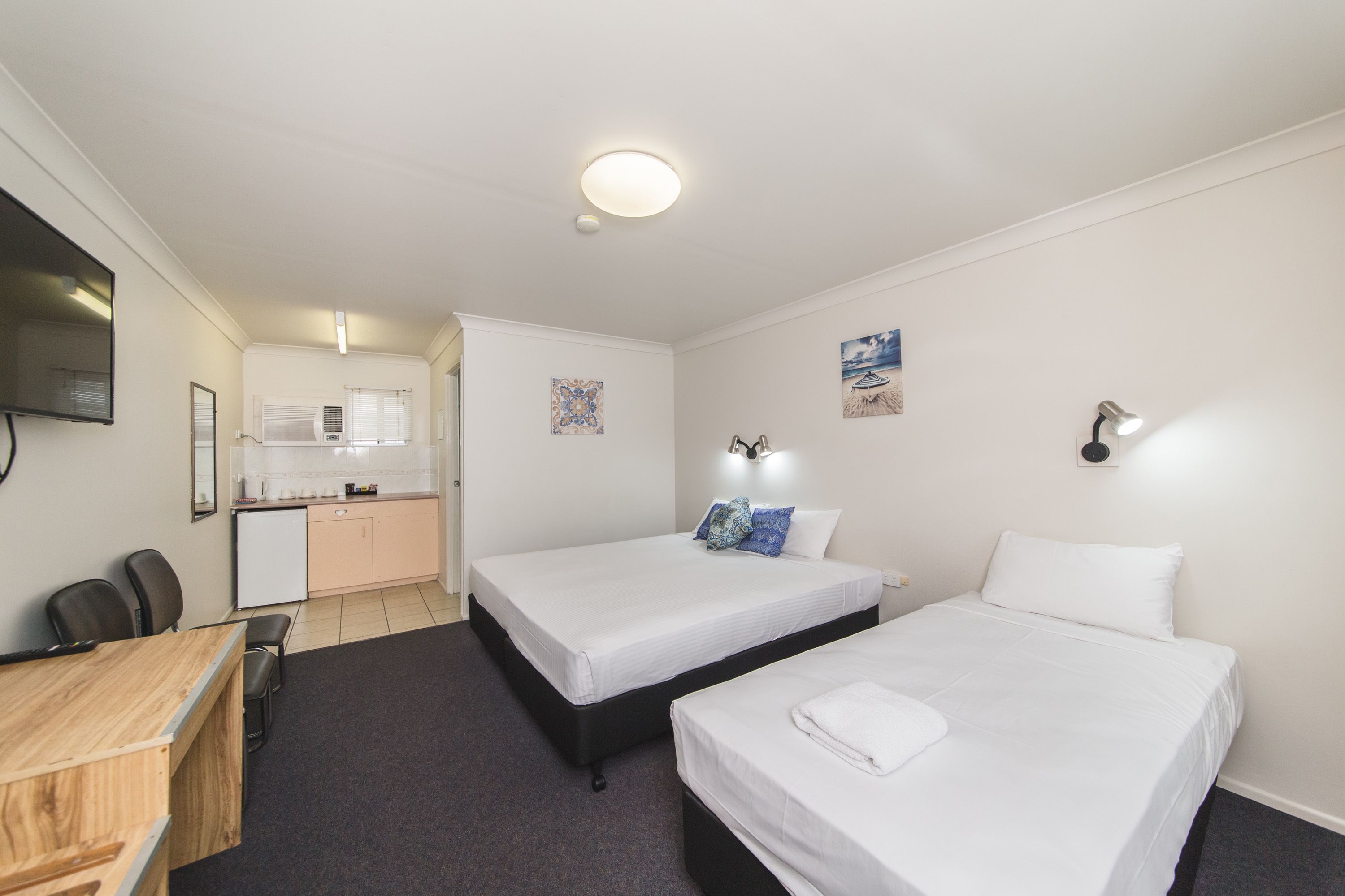 Une chambre d’hôtel avec deux lits, un bureau, une chaise, une télévision et une kitchenette.