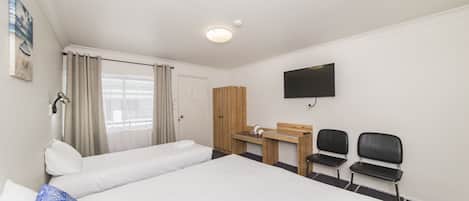 A hotel room with a large bed, a desk with two chairs, a television, and a window with curtains.