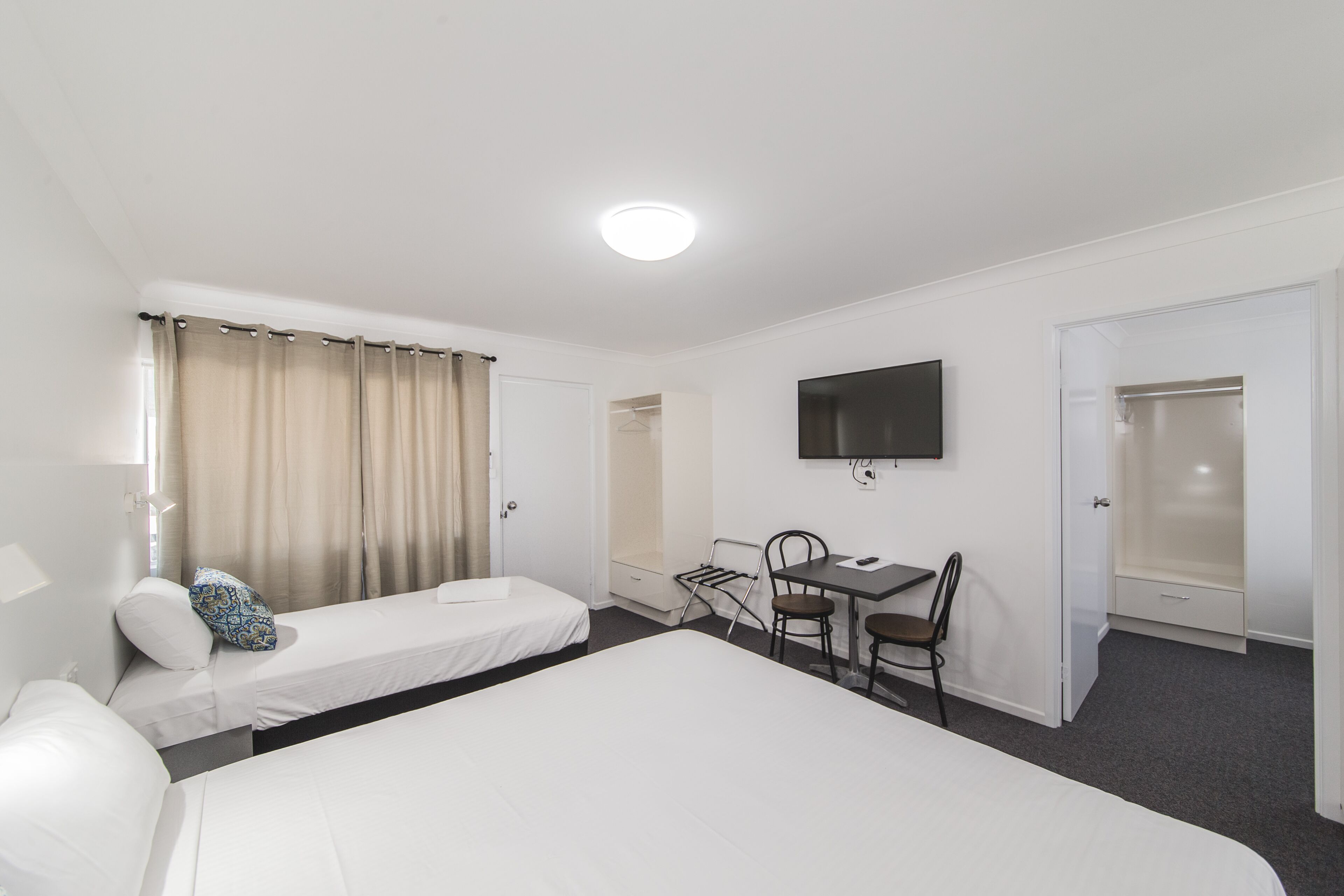 Habitació d'hotel amb dos llits, una taula de treball, una cadira, un televisor i un armari.