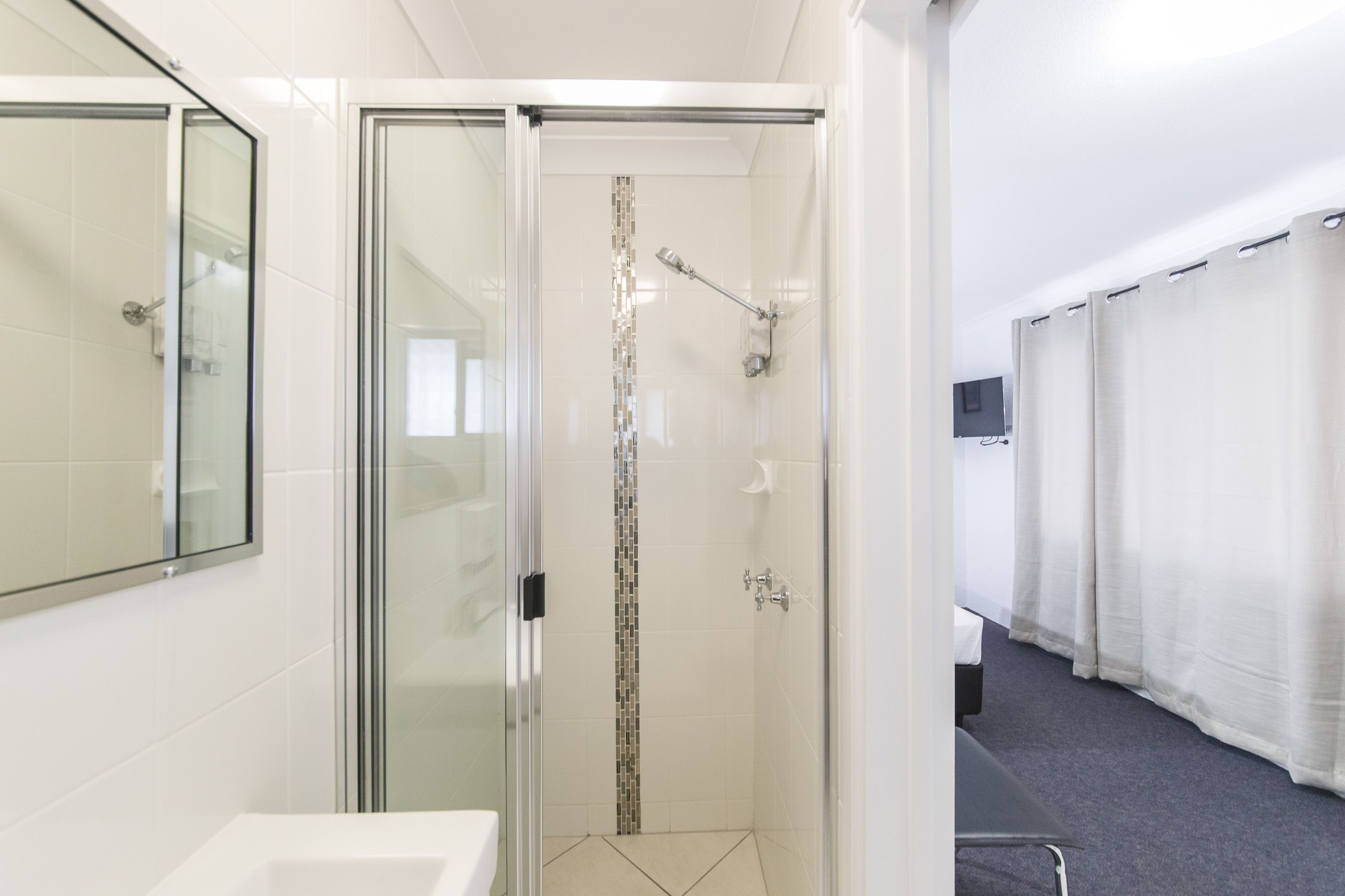 A modern bathroom with a glass-enclosed shower, a white sink, and a mirror.