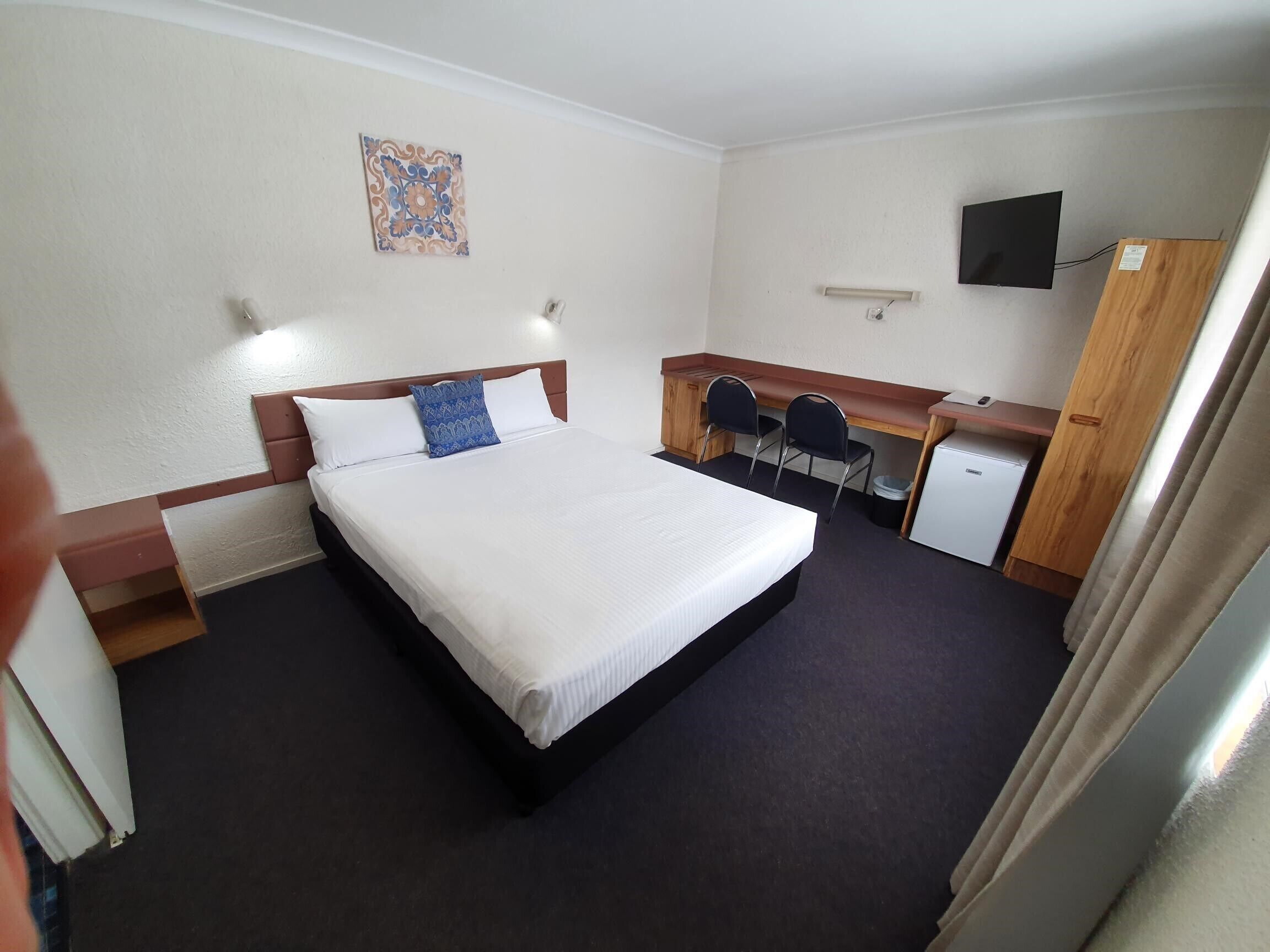 A hotel room with a bed, a desk, a chair, a television, and a small refrigerator.