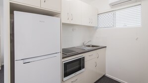 A compact kitchen with white cabinetry, a Haier refrigerator, a microwave, and a sink with a window above. - Metro Motel Rockhampton (Rockhampton)