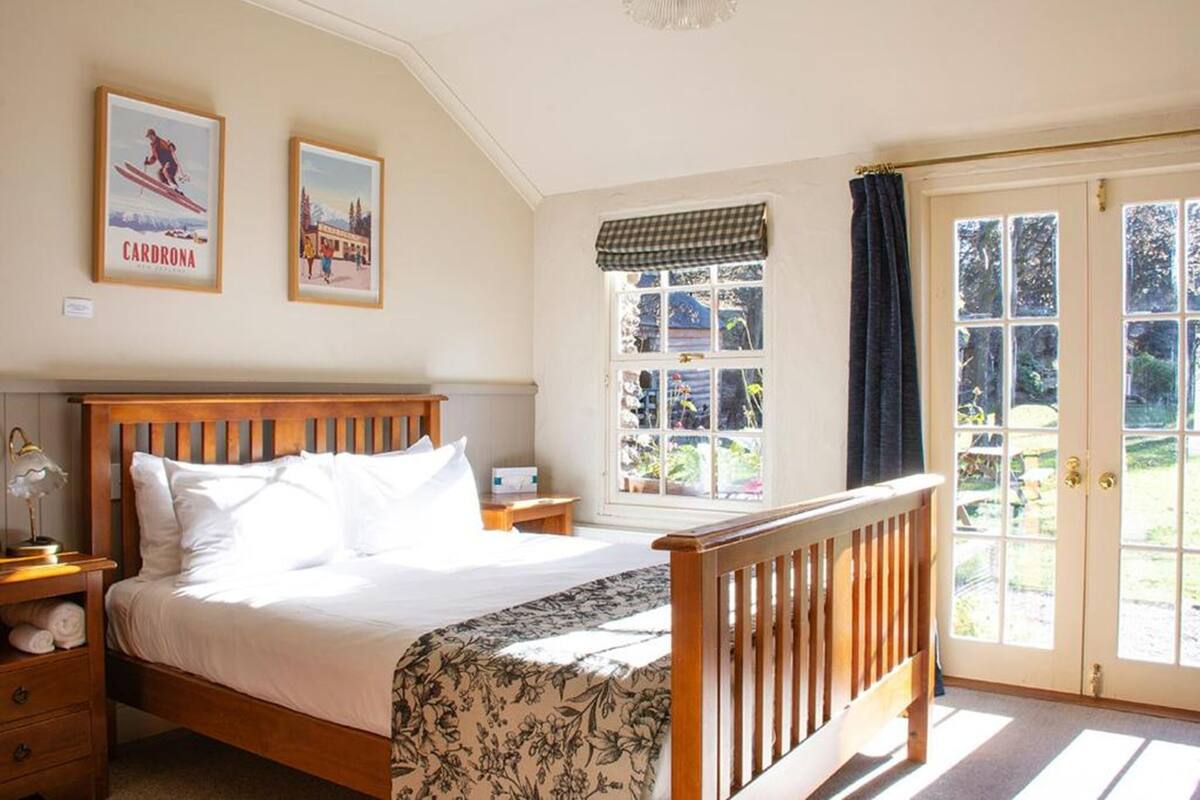 A bedroom with a wooden bed, a nightstand, a window with a view, and two framed pictures on the wall.