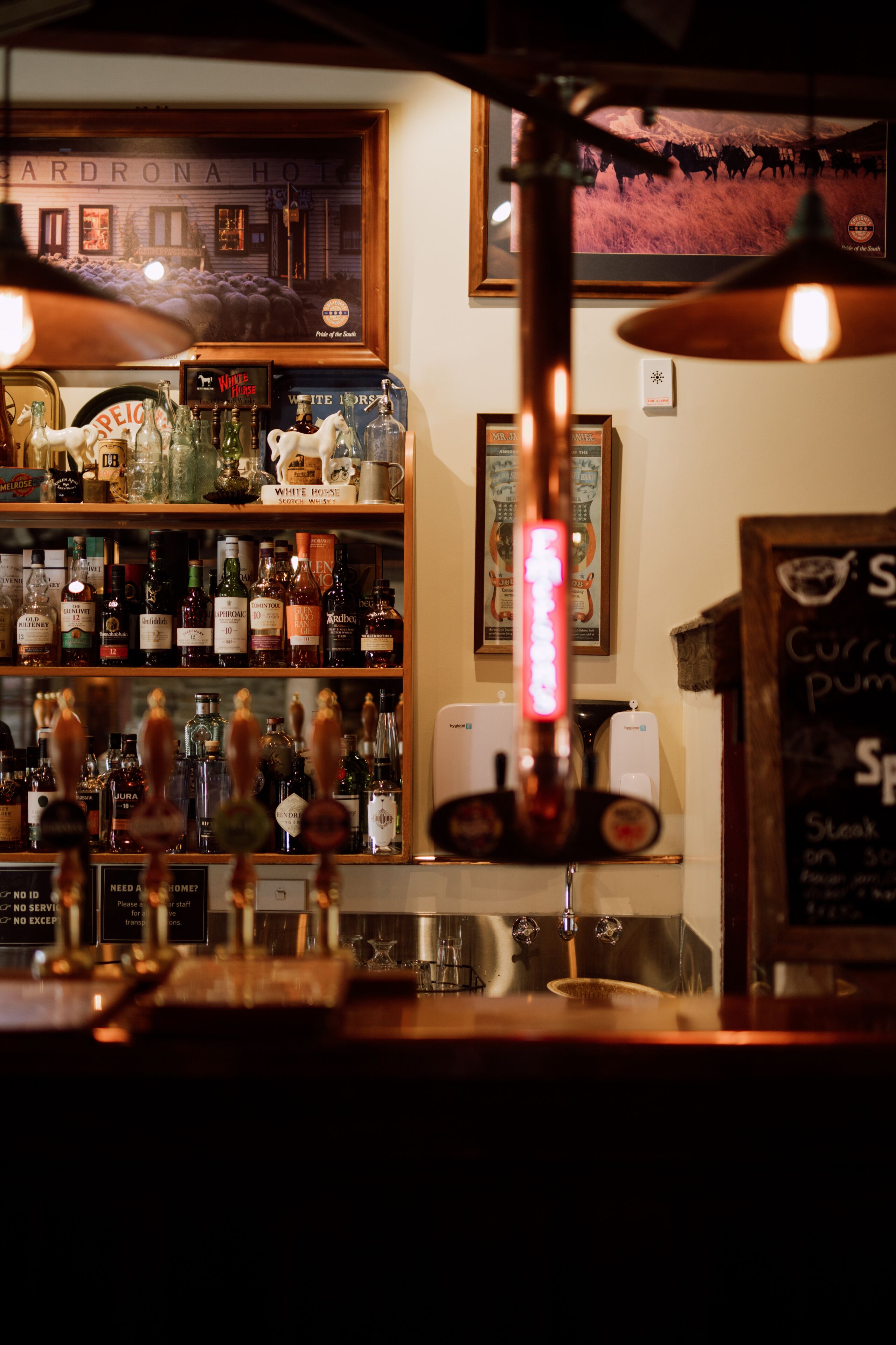 A bar area with shelves of liquor bottles, a beer tap, and a chalkboard menu.
