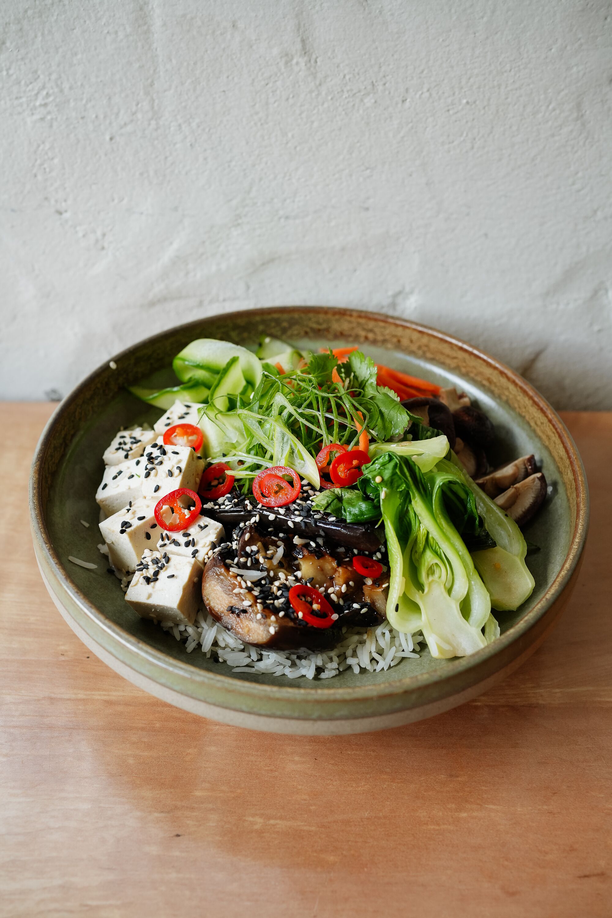 Een schaal eten met rijst, tofu, groenten en sesamzaadjes.
