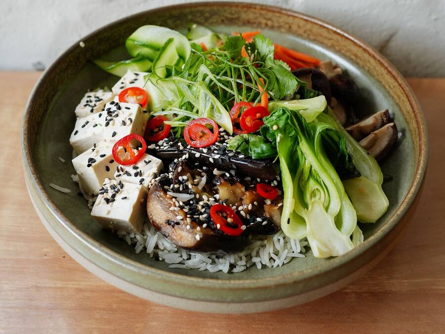 Een schaal eten met rijst, tofu, groenten en sesamzaadjes.