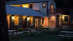 A rustic cabin with stone walls, a metal roof, and wooden deck seating. - Cardrona Hotel (Cardrona)
