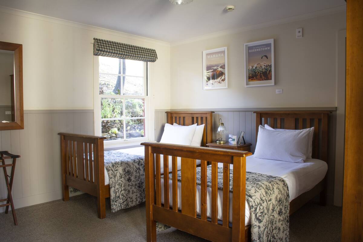 A bedroom with two wooden beds, a window with a checkered valance, and two framed posters on the wall.