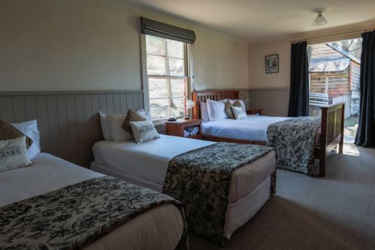 A room with two beds, a bedside table, a lamp, and a window with curtains.