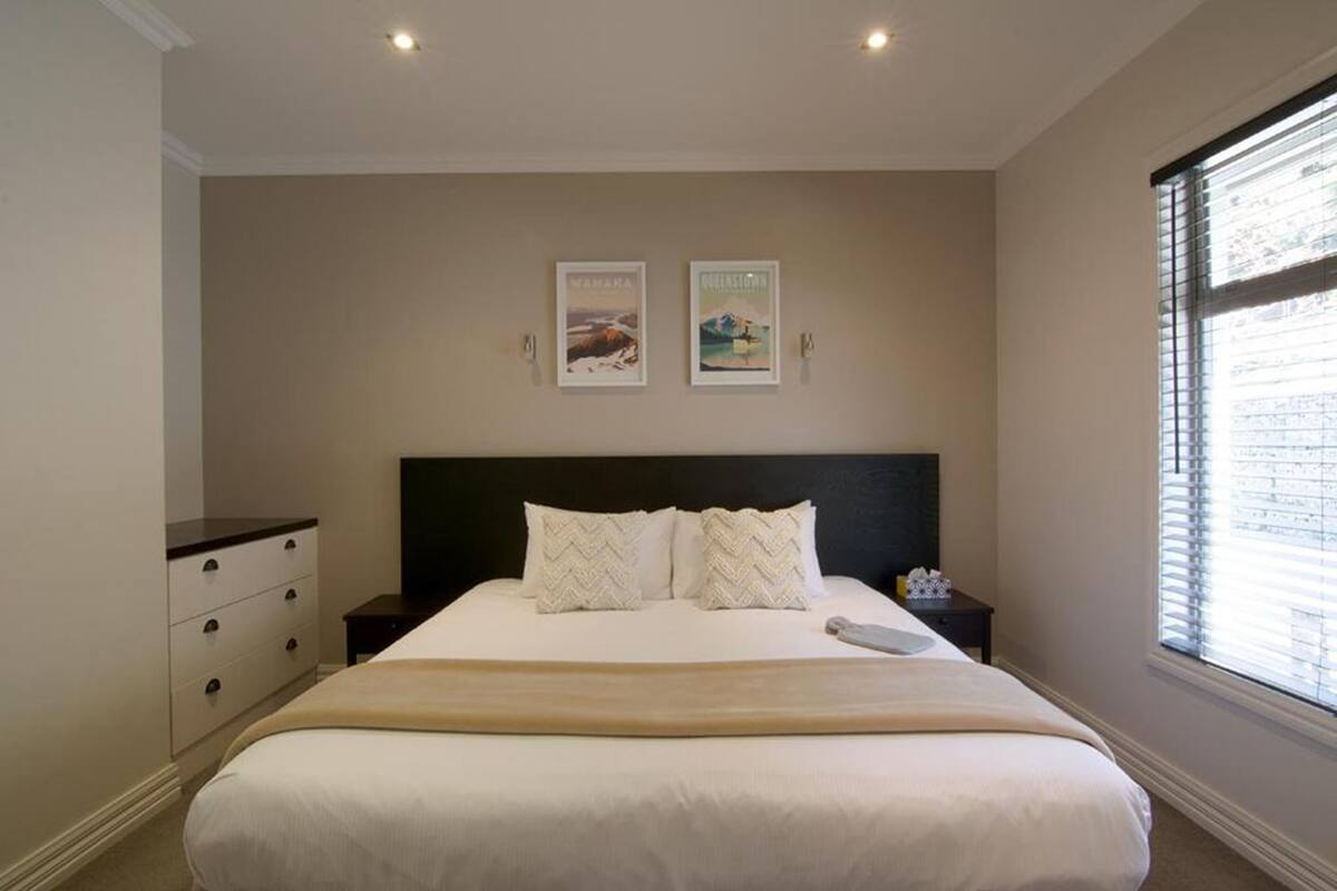 A bedroom with a large bed, a nightstand, a dresser, and two framed pictures on the wall.